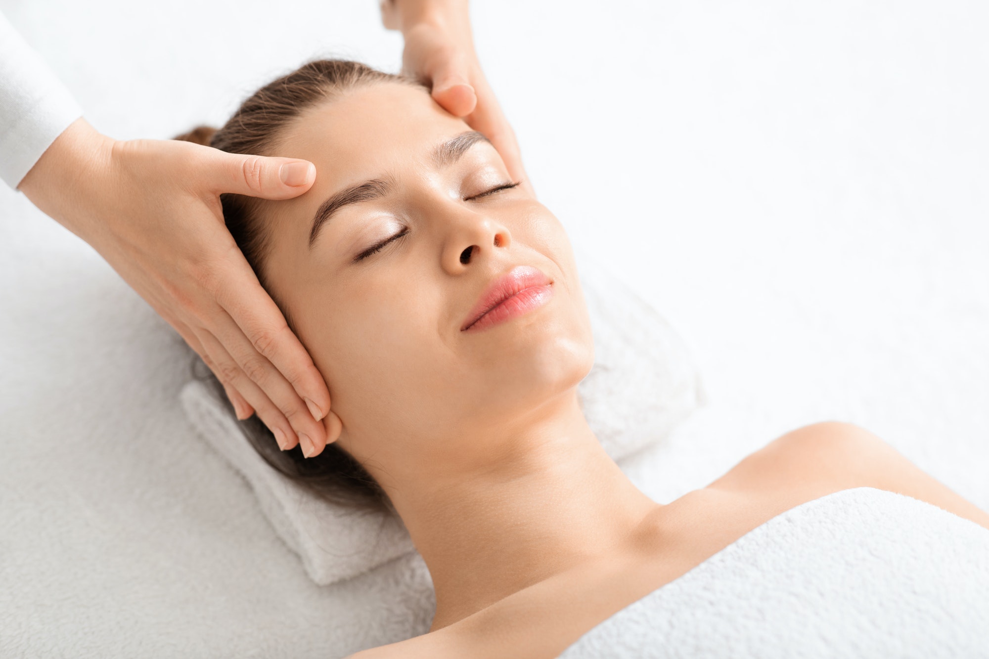 Joyful young woman relaxing during face lifting massage, copy space